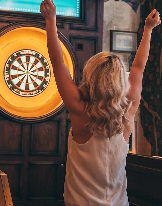 Woman facing a dartboard with her arms raised in celebration